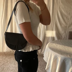 Svart axelremsväska i äkta skinn  - Svart liten väska, bra skick, vintage, axelband och äkta skinn. 