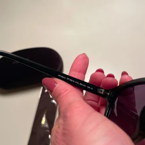 Svarta solglasögon från Tom Ford - Snygga svarta solglasögon från Tom Ford med en klassisk design. De har mörka linser och en stilren båge. Perfekta för att ge en cool touch till din outfit. Kommer med ett matchande fodral.