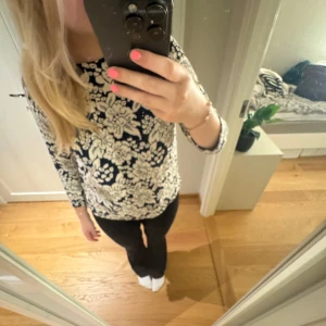 Blommig långärmad topp - Säljer en snygg långärmad topp med blommigt mönster i marinblått och vitt. Perfekt för en stilren look. Toppen har en normal passform och är tillverkad i ett mjukt material.🩷