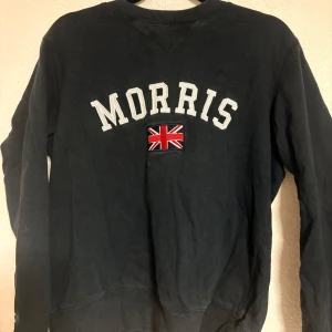 Svart tröja från Morris - Säljer en svart tröja från Morris med broderad text och en Union Jack-flagga på framsidan.