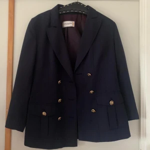 Svart kavaj från Fashion Collection - Snygg svart kavaj från Fashion Collection med dubbelknäppning och guldknappar. Kavajen har en klassisk design med långa ärmar och är perfekt för en stilren look. Materialet är en blandning av polyester och siden för en bekväm passform.