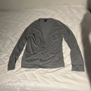 Grå kofta från Filippa K - Säljer en stilren grå kofta från Filippa K i storlek M. Koftan har en v-ringad design med knappar framtill. Koftan är i väldigt bra skicka, inga defekter.