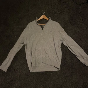Grå tröja från Polo Ralph Lauren - Säljer en stilren grå tröja från Polo Ralph Lauren. Tröjan har en halv dragkedja och är långärmad, perfekt för en avslappnad look. Den är tillverkad i ett mjukt material som ger en bekväm passform.