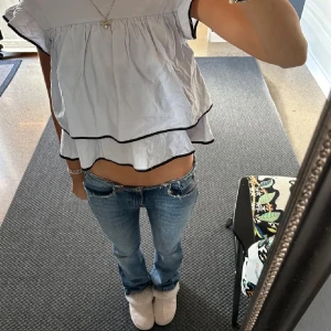 Vit blus med svarta detaljer - Säljer en söt vit blus med svarta kanter och volanger. 