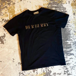 Burberry t-shirt  - Snygg svart t-shirt från Burberry med deras ikoniska logga i mitten. T-shirten är kortärmad och gjord i mjukt material för extra komfort. Passar både till vardags och fest!