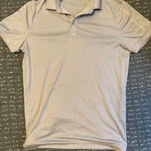 Beige pikétröja från J.Lindeberg - Snygg beige pikétröja från J.Lindeberg i regular fit. Tillverkad i 100% polyester med klassisk krage och knappar framtill. Perfekt för en stilren look.