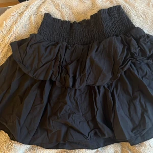 Svart volangkjol - Snygg svart kortkjol med volangdetaljer och elastisk midja. Perfekt för en trendig look.