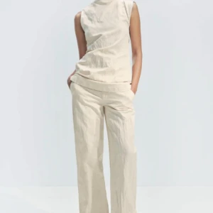 Beige linnebyxor modell skrynkliga raka byxor mid rise midja  - Stilrena beige linnebyxor med en rak passform. Byxorna är vida i benen.  