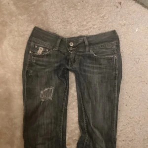 Mörkblå jeans med slitningar - Snygga mörkblå jeans med slitningar på framsidan. De har en låg midja och en bootcut-stil. 