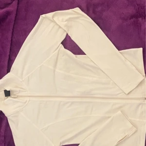 Vit långärmad tröja från Gina Tricot - Säljer en stilren vit långärmad tröja från Gina Tricot. Tröjan har en dragkedja framtill och är tillverkad i ett mjukt material. Perfekt för en enkel och snygg look. Passar bra till både jeans och kjol.