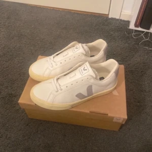 Vita sneakers från Veja - Snygga vita sneakers från Veja med grå detaljer. Skorna har en klassisk design med snörning och en bekväm passform. Perfekta för en stilren look.