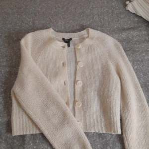 Vit stickad kofta Lindex - Säljer en mysig vit stickad kofta från Lindex i storlek XS. Koftan har långa ärmar och knäpps med stora knappar framtill. Perfekt för kyliga dagar och ger en stilren look.