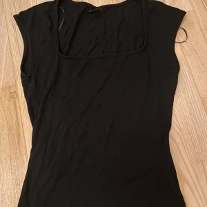 Svart topp från Gina Tricot - Säljer en stilren svart topp från Gina Tricot. Toppen har en enkel design med korta ärmar och en fyrkantig halsringning. Perfekt för en minimalistisk look. Använt ett fåtal gånger! Pris kan diskuteras.