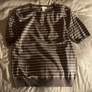 Grå och vit randig tröja - Säljer en stilren grå och vit randig tröja med korta ärmar. Perfekt för en avslappnad look. Tröjan har ribbade kanter vid ärmslut och nederkant.