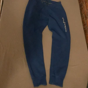 Blå mjukisbyxor från Sail Racing storlek M - Snygga blå mjukisbyxor från Sail Racing med snörning i midjan och logga på benet. Perfekta för en avslappnad stil. De har en bekväm passform och är gjorda i mjukt material.