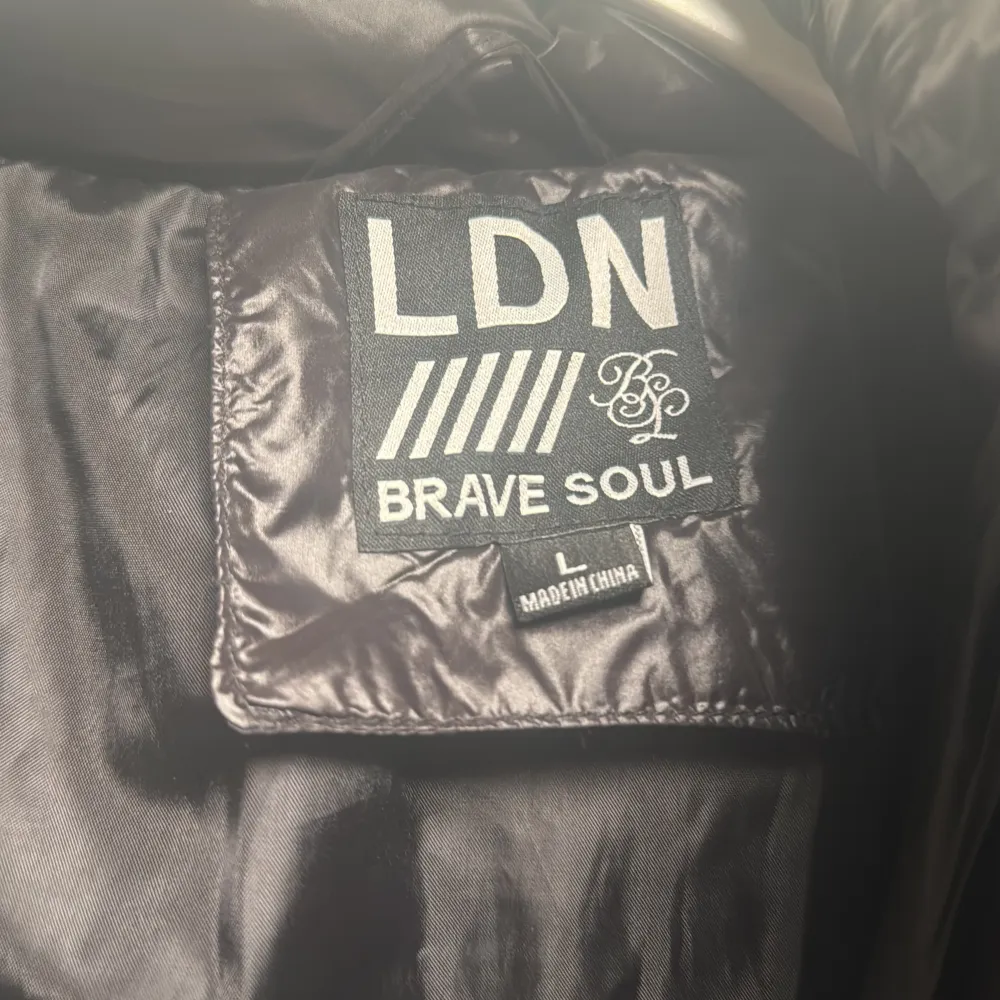 Säljer en svart pufferjacka från Brave Soul. Jackan har en glansig yta och är utrustad med dragkedja och flera fickor. Perfekt för kyligare dagar med sin vadderade design.. Takit.