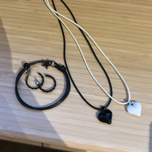 Smyckeset med hjärthalsband och stjärnarmband - Säljer ett stilrent smyckeset med två halsband ett armband och två örhängen. Halsbanden har hjärtformade hängen i svart och vitt, medan armbandet är svart med en stjärndetalj. Perfekt för att komplettera din look!