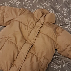Beige pufferjacka - Säljer en beige pufferjacka med långärmad design. Jackan har en quiltad stil och är perfekt för kyligare väder. Den har en dragkedja framtill och en hög krage för extra värme. Perfekt för att hålla sig varm och stilren under vintern.