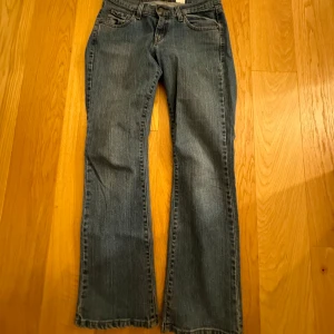 Blå jeans från Levi's - Säljer ett par klassiska blå Levi's jeans med bootcut-stil. De har en låg midja och är tillverkade i jeansmaterial. Perfekta för en avslappnad look.