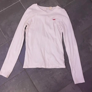 Vit långärmad tröja från Levi's - Säljer en klassisk vit långärmad tröja från Levi's med en liten röd logga på bröstet. Perfekt för en stilren och avslappnad look. Tröjan är i bomull och har en normal passform.