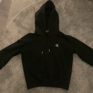 Svart hoodie från Calvin Klein Jeans - Säljer en stilren svart hoodie från Calvin Klein Jeans med en liten CK-logga på bröstet. Den har en justerbar huva med dragsko och långa ärmar. Perfekt för en avslappnad look. Köpt för ca 1000 kr. Hör av dig vid funderingar💕