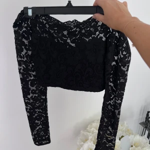Långärmad crop top med spets - En långärmad svart crop top med spets. Toppen är off-shoulder. Ryggen och ärmarna är helt i spets. Använd max 3 gånger 💞💞  Längd: 28 cm Axel: 43 cm Armlängd: 63 cm Midja: 58 cm