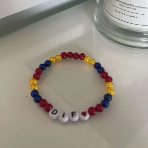 Färgglatt pärlarmband med bokstäver - Säljer ett supercoolt armband med färgglada pärlor i rött, blått och gult. Armbandet har vita pärlor med bokstäverna 'DIF' och ett litet hjärta. Perfekt för att ge en personlig touch till din outfit!