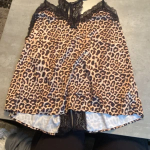 Leopardmönstrad linne med spetsdetaljer - Säljer en snygg leopardmönstrad linne med svarta spetsdetaljer. Den har en liten rosett framtill och är perfekt för en festlig kväll. Materialet känns silk och lyxigt.