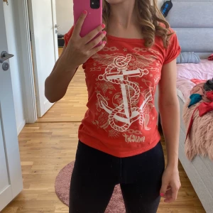 Röd t-shirt med ankarmotiv från Insight - Säljer en cool röd t-shirt från Insight med ett stort vitt ankarmotiv och en orm på framsidan. T-shirten har en normal passform och korta ärmar, perfekt för en avslappnad stil. Den är i bra skick och redo för nya äventyr!