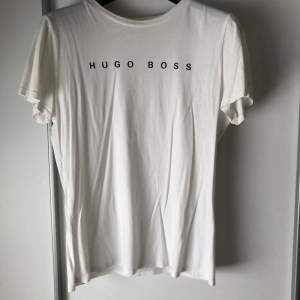 Säljer en vit t-shirt från Hugo Boss. Den har korta ärmar. Perfekt för en avslappnad och snygg look. Hugo Boss-loggan är tryckt både fram och bak på tröjan. Knappt använd