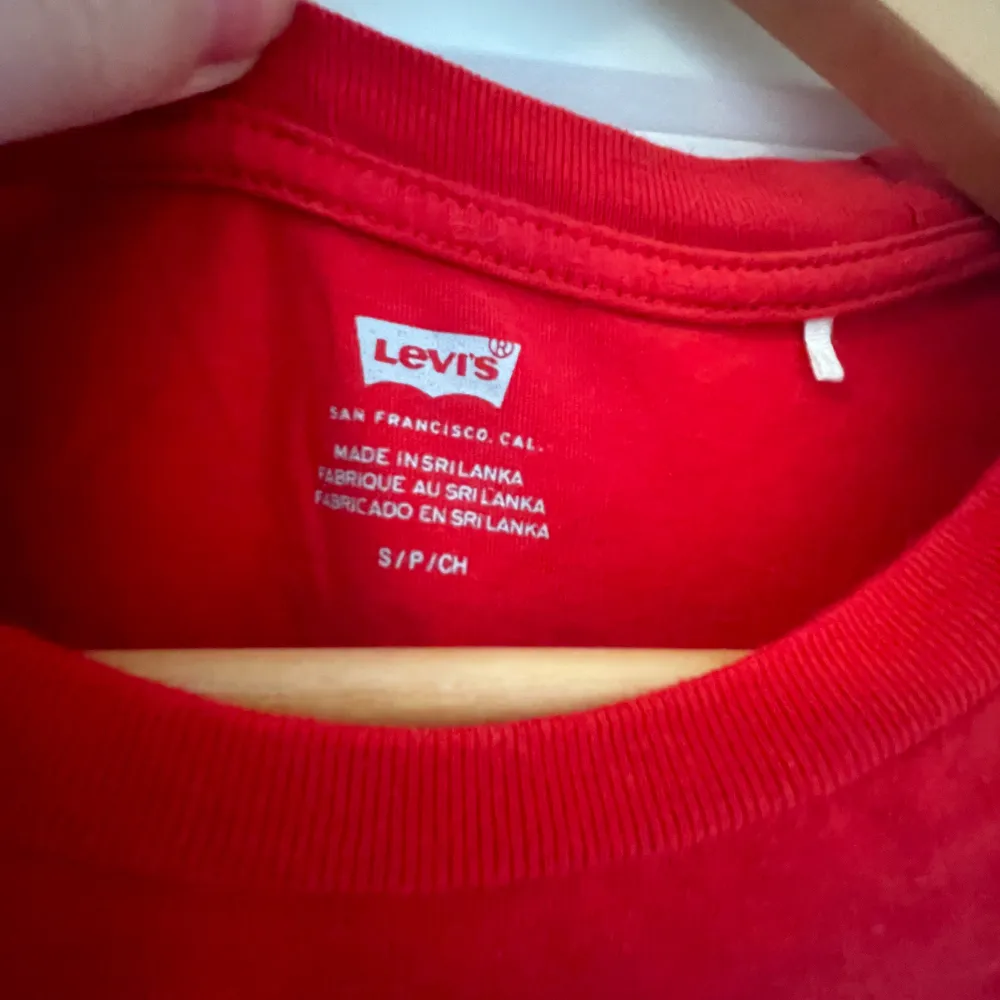 Säljer en snygg röd t-shirt från Levi's med deras ikoniska logga i vitt på bröstet. Perfekt för en casual look och passar till det mesta. T-shirten är i bomull och har korta ärmar. Perfekt för sommardagar eller som en del av en lager-på-lager outfit.. T-shirts.