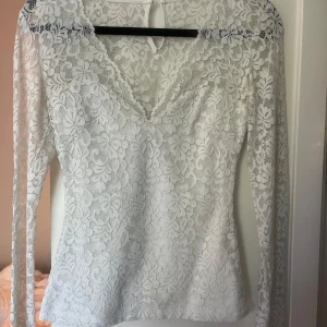 Vit spetsblus - Säljer en superfin vit spetsblus med långärmad design. Blusen har en v-ringad stil och är helt täckt i ett vackert blommigt spetsmönster. Perfekt för både fest och vardag!