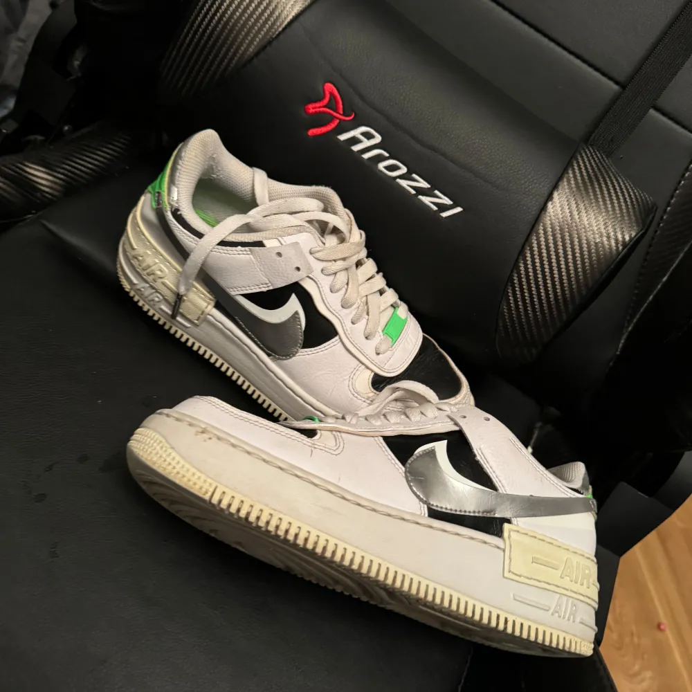 Säljer ett par Nike Air Force sneakers i vitt och svart med coola gröna detaljer. Skorna har en klassisk design med snörning och en bekväm passform. Perfekta för vardagsbruk och ger en stilren look.. Skor.