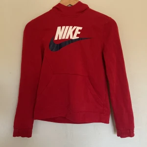 Röd hoodie från Nike - Säljer en snygg röd hoodie från Nike. Den har en stor Nike-logga i vitt och svart på framsidan och en praktisk ficka. Perfekt för höst och vinter med sin mysiga känsla. Passar både till träning och vardag.