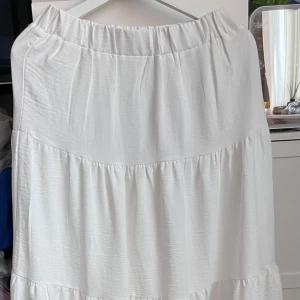 Vit långkjol - Säljer en superfin vit långkjol som är perfekt för sommaren! Kjolen har en luftig och bekväm passform med elastisk midja. Den är gjord i ett lätt och flödande material som ger en härlig känsla. Perfekt för både vardag och festliga tillfällen!