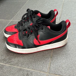 Svart och röd Nike sneaker - Säljer ett par snygga Nike sneakers i svart och rött. Skorna har en klassisk design med snörning och en vit sula. Perfekta för vardagsbruk eller träning. De är i bra skick med lite slitage på sulan.