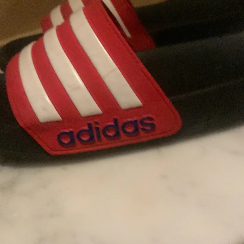 Säljer ett par snygga Adidas sandaler i rött och vitt. De har de klassiska tre ränderna och Adidas-loggan på sidan. Perfekta för sommaren eller att ha på stranden. De är i bra skick och redo för nya äventyr!. Skor.