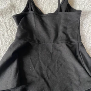 Svart klänning från Ginatricot - Säljer ett stilrent svart linne från Ginatricot. Den har smala axelband och en figurnära passform som ger en snygg siluett. Perfekt för festliga tillfällen eller en utekväll. linnet är i bra skick och aldrig använt mer än 1 gång!