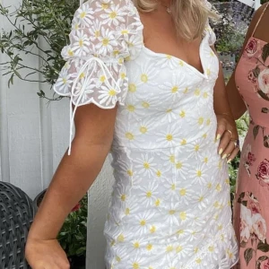 Blommig klänning - Klänning från märket Love Triangle. Superfin i vit spets med gula blommor. Endast använd 1 gång. Ordinare pris ca 800kr. 