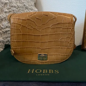 Läderväska - Äkta läderväska från Hobbs London. Ljusbrun i croco-mönster.  Använd fåtal gånger. Inga defekter men ett extra hål i remmen så den också kan bäras på axeln. Pris kan diskuteras. Hör av dig om du har frågor💓