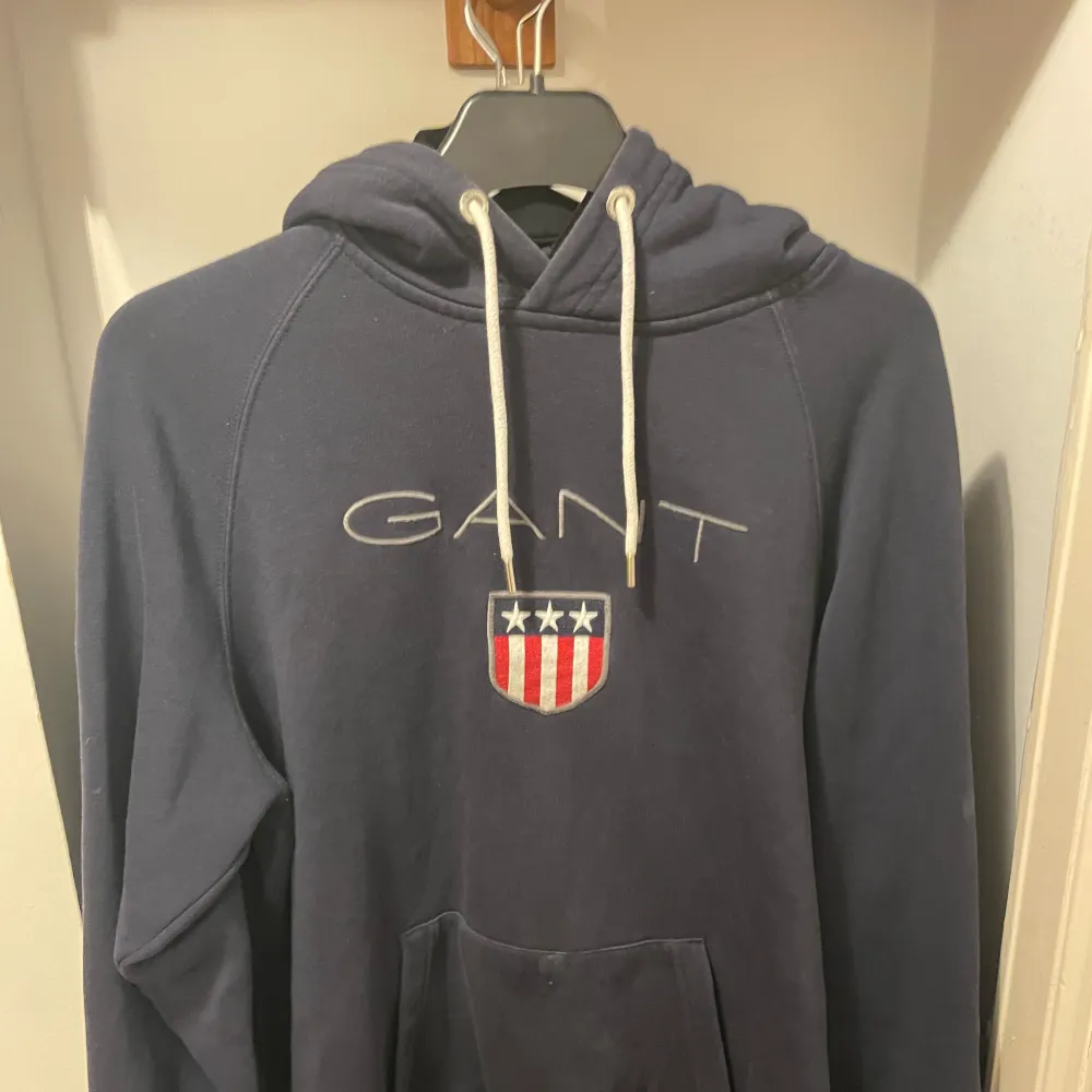 Säljer en klassisk och bekväm marinblå hoodie från GANT i storlek L med en mjuk insida som håller dig varm och bekväm. GANT är känt för sin kvalitet, och denna hoodie är inget undantag. Den är i mycket gott skick, utan några tecken på slitage. . Hoodies.