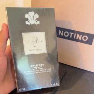 Creed Aventus Parfym - Säljer en lyxig och elegant parfym från Creed, Aventus. Flaskan är på 100 ml och kommer i en stilren svart förpackning med silverdetaljer. Aventus är känd för sin unika och kraftfulla doft som passar perfekt för speciella tillfällen. Förpackningen har en klassisk design med Creed-loggan och texten 'De père en fils depuis 1760'. Den är helt oöppnad!