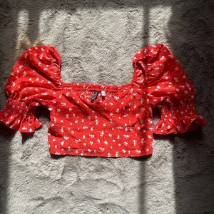 Röd magtröja med vitt blommigt mönster  - Kortare tröja med puffiga ärmar och har ett blommigt mönster 