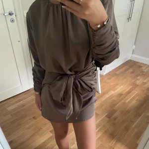 Satin klänning i champagnefärg - En jätte fin champagnefärgad klänning från Gina Tricot, där man kan välja knuta en rosett framåt eller bakåt. Använd endast en gång. 