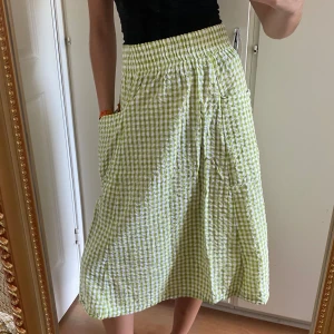 Rutig somrig kjol - Grön och vitrutig kjol. Fickor på sidorna, resårmidja ocjh tyget har lite textur. Tunn och bekväm.