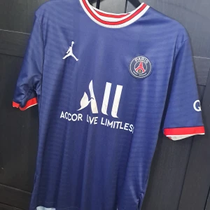 Blå PSG fotbollströja från Jordan - Jag Säljer en snygg blå PSG fotbollströja från Jordan med korta ärmar och snygga röda och vita detaljer. Tröjan har klubbens emblem på bröstet och Ligue 1-märke på ärmen. Perfekt för alla fotbollsfans som vill visa sitt stöd för laget! ⚽️ det är lite fläckar fram men syns knappt. Den är ett halv år gammal  och är i storlek s. Den har en stor passform men på ett bra sätt. 👍Den är gjord i Thailand. Och redo för nya tag. Ny pris 500kr men jag säljer den för 150kr bara för att det är Jordan märket. 🔥