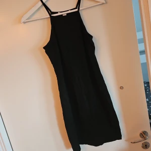 Svart ärmlös klänning - Snygg svart ärmlös klänning med smala axelband. Perfekt för en stilren look. Klänningen har en enkel och elegant design som passar till många tillfällen.