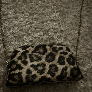 Leopardmönstrad axelväska med kedja - Snygg axelväska med leopardmönster och guldfärgad kedja. Väskan har en dragkedja upptill och flera fack inuti för enkel organisering. Perfekt för att ge din outfit en trendig touch.💕💕