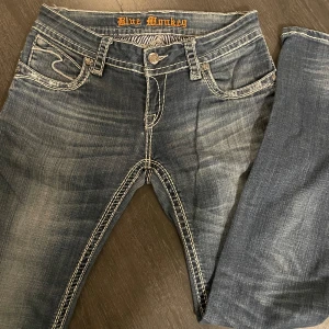 Blå jeans från Blue Monkey - Snygga blå jeans från Blue Monkey med kontrastsömmar och unikt broderi på bakfickorna. W29 L32 mått: midjemått 40cm, innerbenslängd 82cm