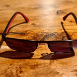 Svarta solglasögon från Emporio Armani - Snygga svarta solglasögon från Emporio Armani med röda detaljer på skalmarna. De har en modern, rektangulär form och är perfekta för en stilren look. Märkesloggan syns tydligt på sidan av skalmen.